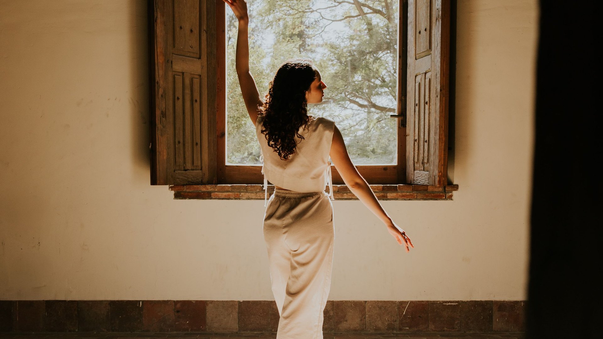A dancer reaching toward a sunlit window